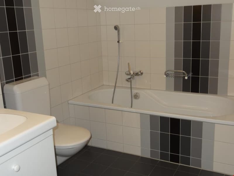 Modern bathroom with white tiles, black accents, bathtub, toilet, and showerhead.