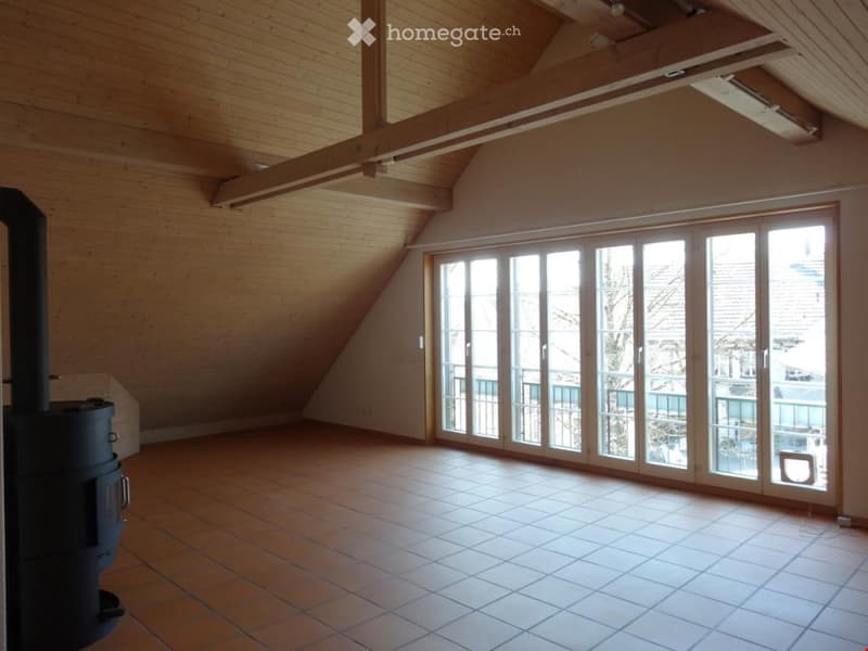 Empty room with wooden ceiling beams, large sliding glass doors leading to a balcony, tiled floor, and a wood-burning stove.