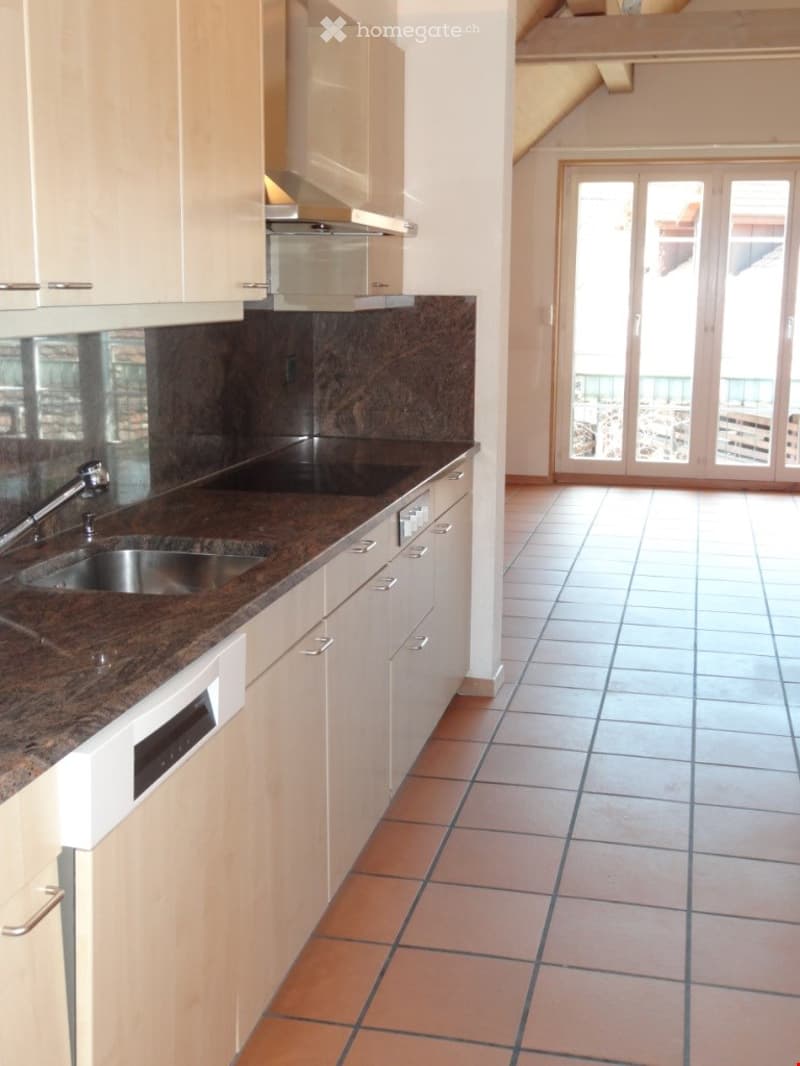 Modern kitchen with white cabinets, granite countertop, stainless steel sink, dishwasher, and range hood. Large sliding glass doors lead to a balcony.