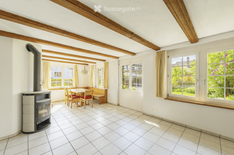 Bright room with exposed wooden beams, fireplace, dining table with chairs, and bench seating.