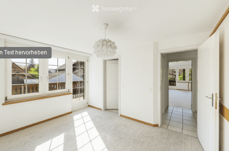 Bright, empty room with large windows, white walls, and a modern pendant light fixture. The space is unfurnished, showing only the base structure and flooring.