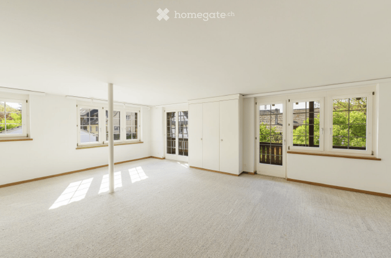 Completely empty room with white walls, large windows, and a white column in the center. No furniture or equipment.