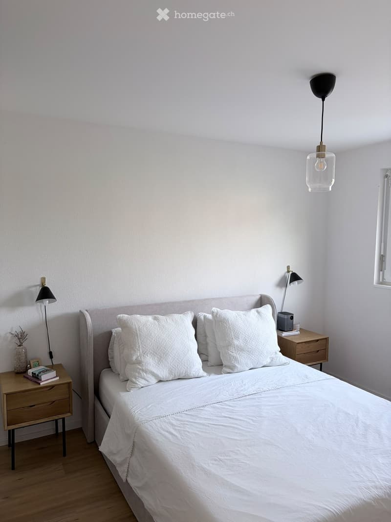 A modern, minimalist bedroom with a neatly made bed, two nightstands, lamps, and decorative items.