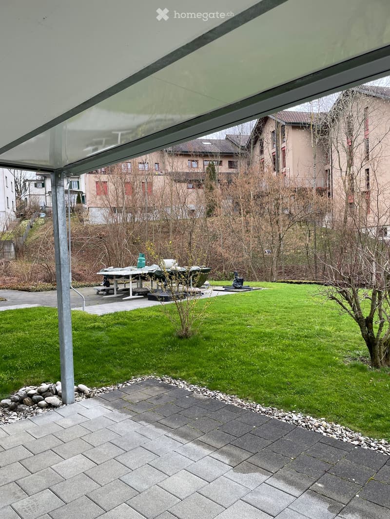 Garden area with a paved patio, grassy lawn, and a covered outdoor seating area with a table and benches.