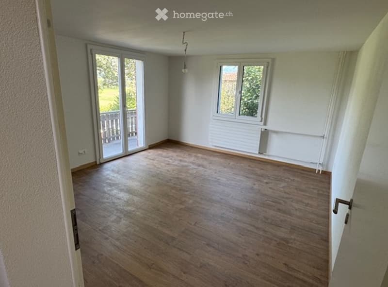 Empty room with wooden flooring, large window, and sliding glass door leading to a balcony.