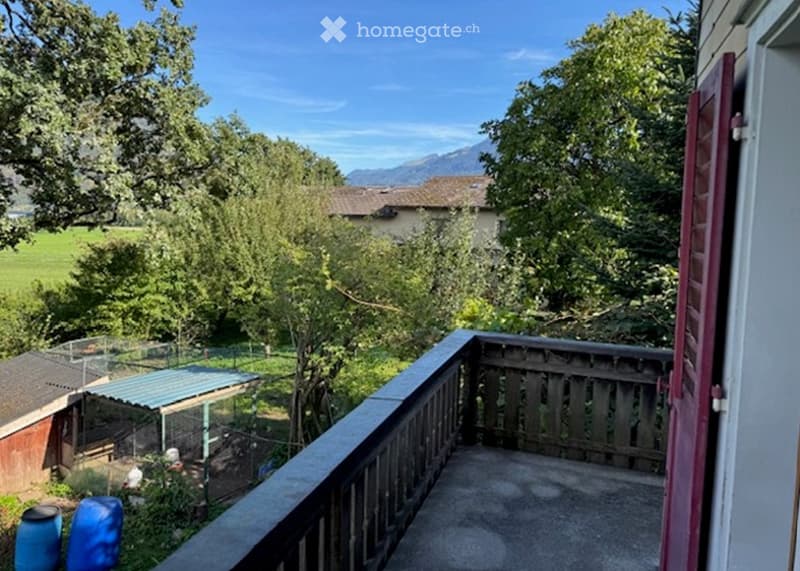 Balcony overlooking a lush garden and distant mountains, with wooden railing and a view of the surrounding landscape.