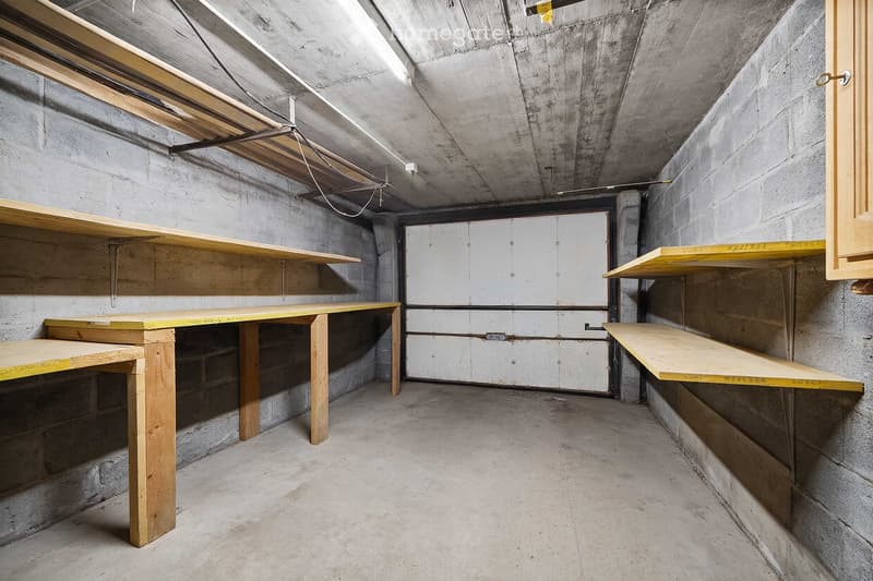 Empty basement or storage room with concrete walls and floor, wooden shelves, and exposed ceiling beams.