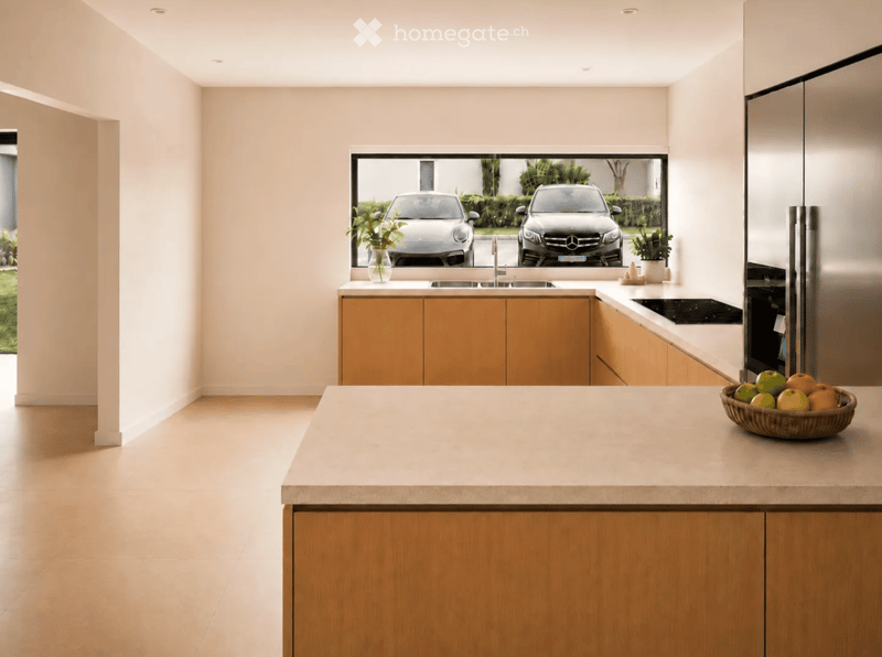 Modern kitchen with light wooden cabinets, a central island, and a large window overlooking a driveway with parked cars.