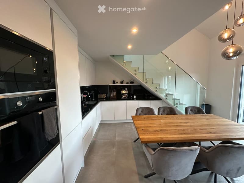 Modern kitchen with white cabinets, a wooden dining table, four chairs, a built-in oven, and a staircase leading to another level.