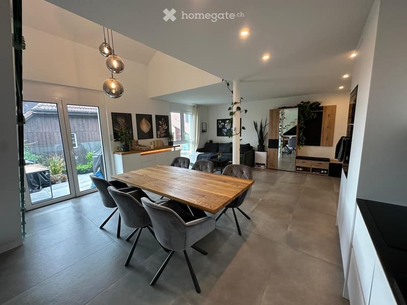 Open-plan living and dining area with modern furniture, large windows, and pendant lights.