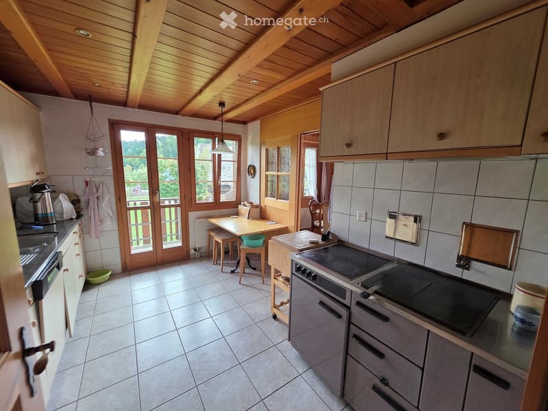 Bright kitchen with wooden beams, large windows, and a dining area. Features a modern electric stove, sink, and ample cabinetry.