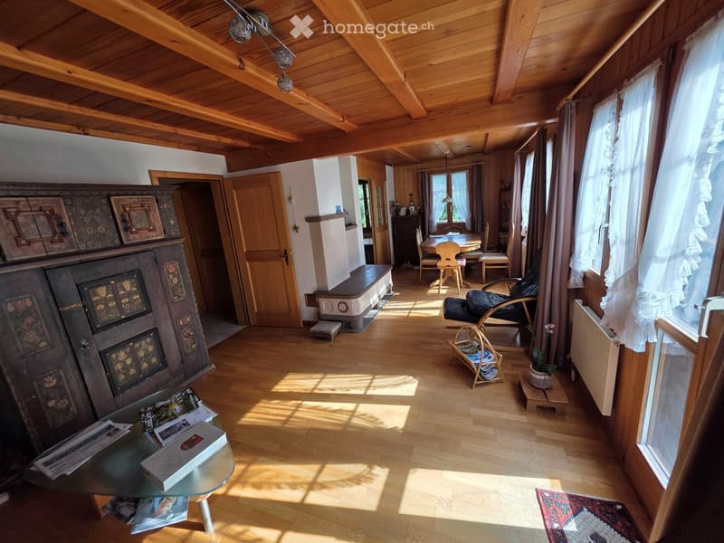 Bright living room with wooden beams, large windows, a glass coffee table, a sofa, a fireplace, and a dining area with a table and chairs.