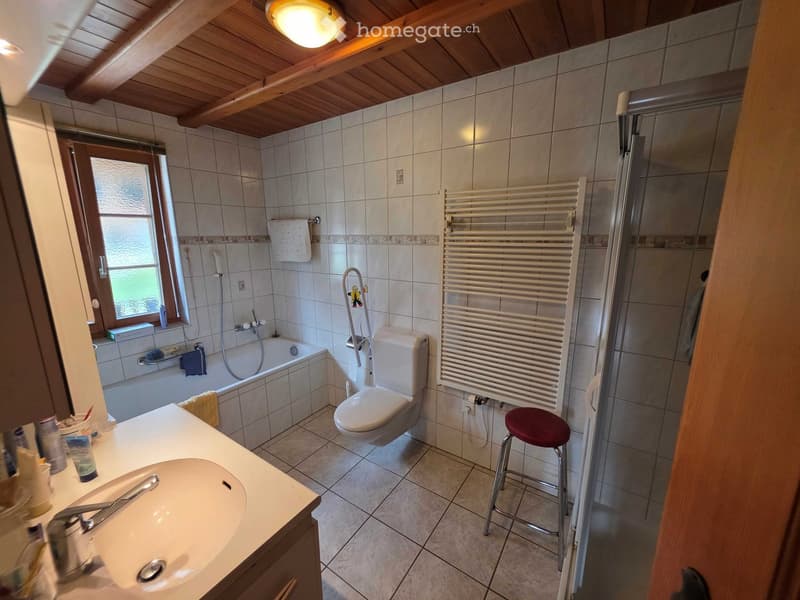 Bathroom with a sink, toilet, bathtub, shower, radiator, and a small window. Wooden ceiling and tiled walls.