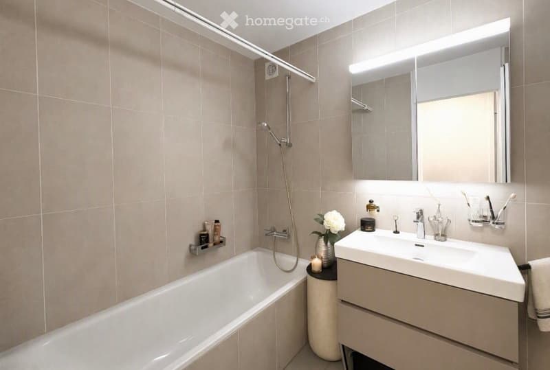 Modern bathroom with a bathtub, sink, large mirror, and shower. Includes a flower vase, candle, and toothbrush holder.