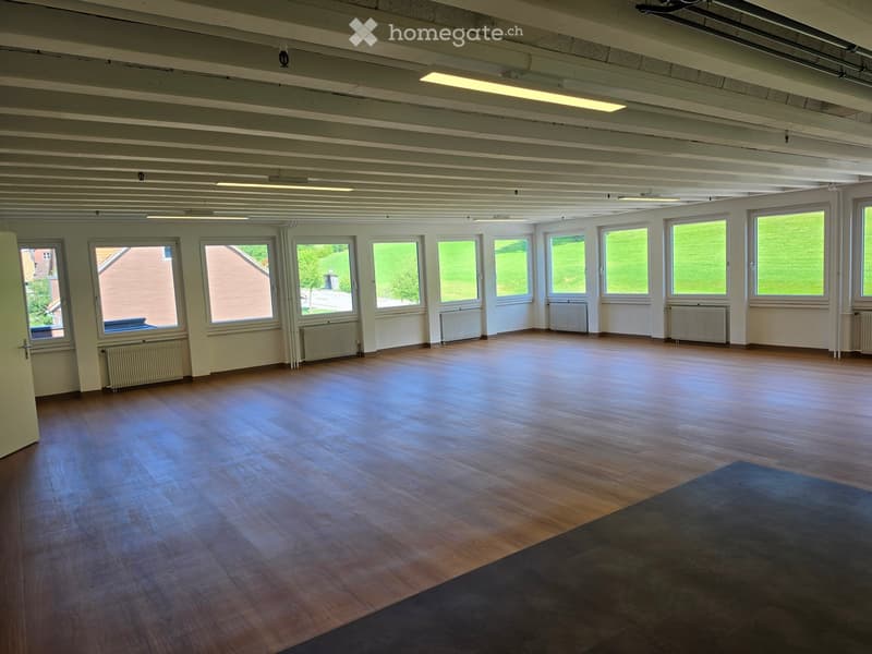 Empty room with wooden flooring, large windows, radiators, and exposed ceiling beams.