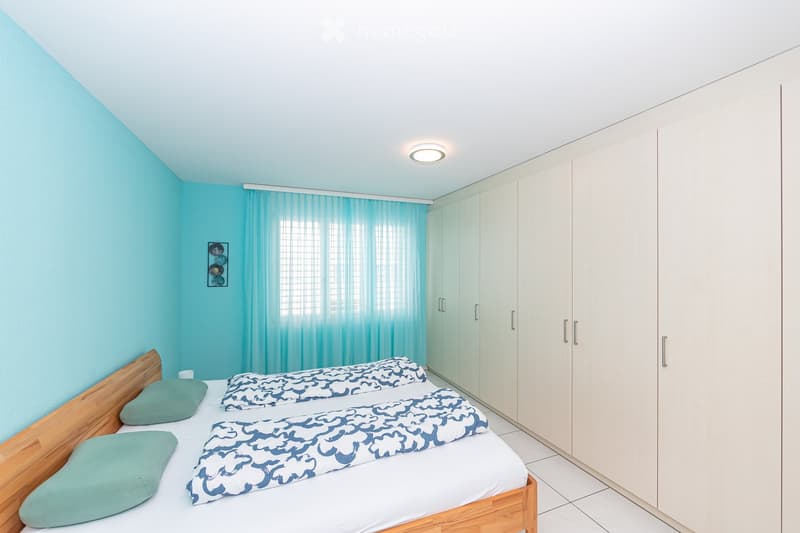 Bright bedroom with two single beds, light blue walls, white wardrobe, and sheer curtains.