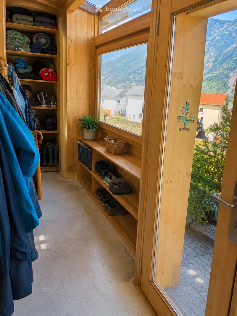 Wooden hallway with built-in shoe rack, coat rack, and storage shelves, leading to a scenic mountain view through large windows.