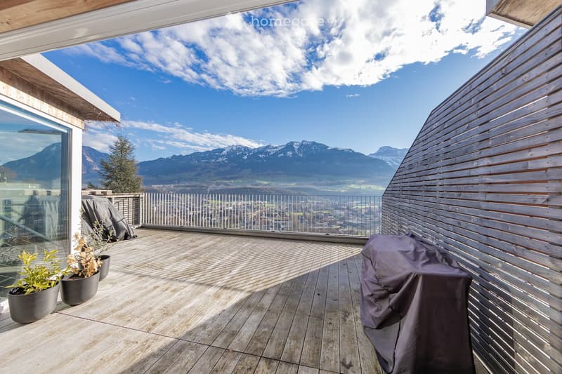 Wooden deck terrace with a panoramic mountain view, covered seating area, and potted plants.