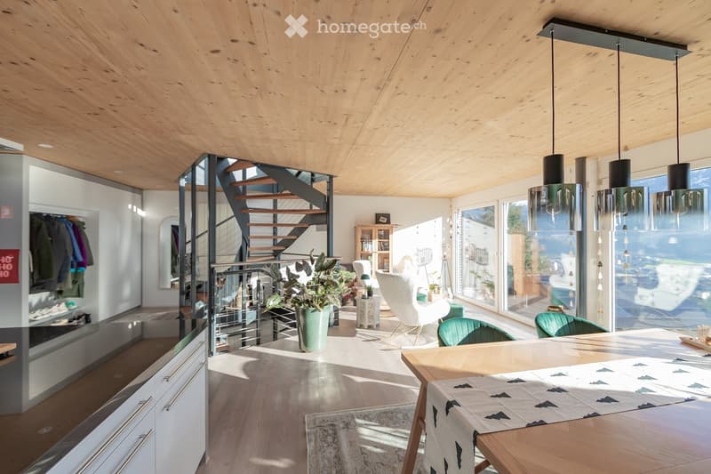 Open-plan living and dining area with wooden ceiling, pendant lights, modern furniture, and large windows offering a view.