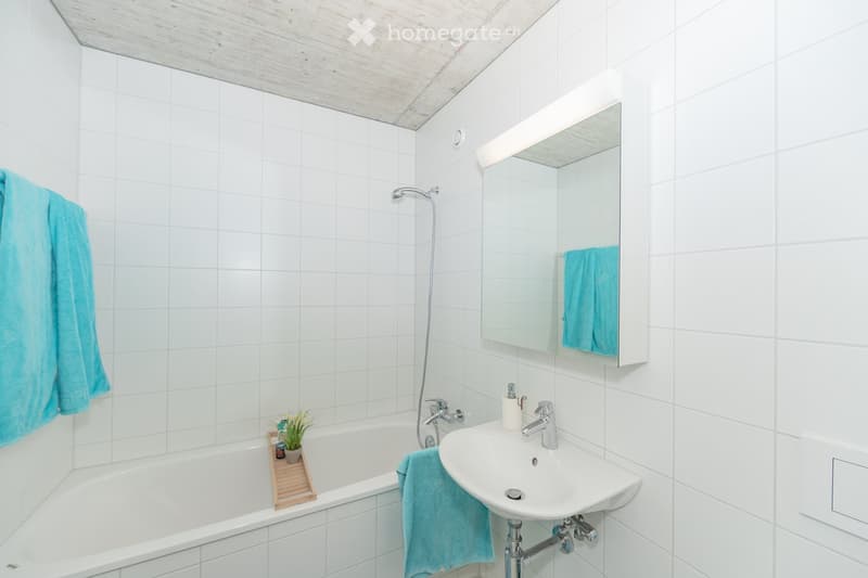 Modern bathroom with white tiled walls and ceiling, featuring a bathtub, sink, mirror, and towel.