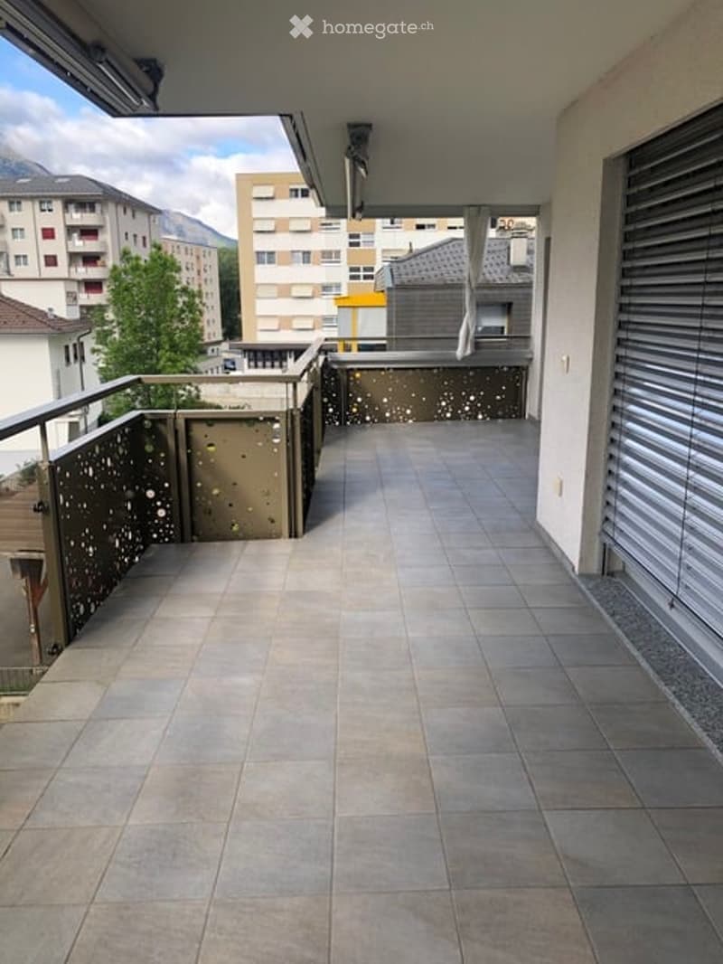 Balcony with tiled floor, metal railing, and view of surrounding buildings and mountains.
