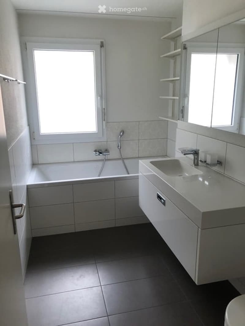 Modern bathroom with white tiles, a bathtub, a sink with a mirror, and a window for natural light.