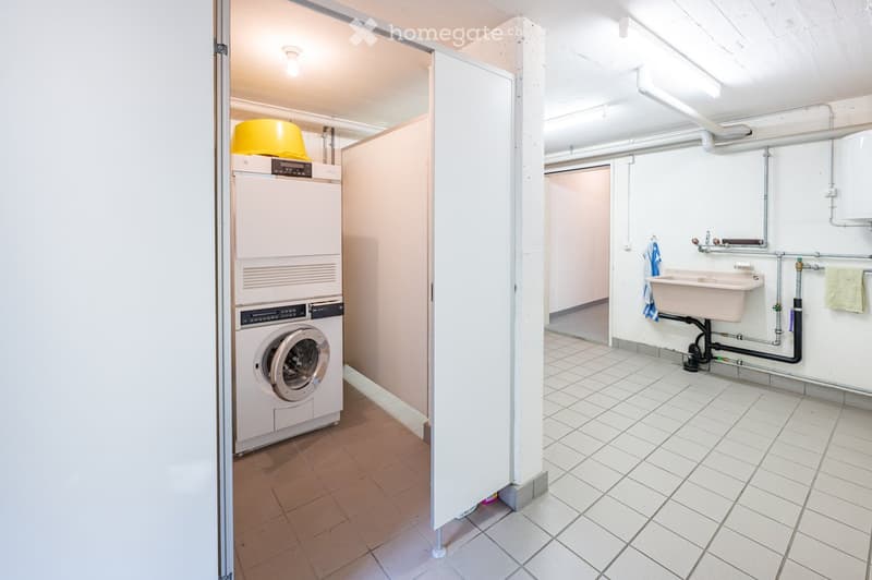 Clean, tiled bathroom with a private washing machine, a sink, and a towel hanging on the wall.
