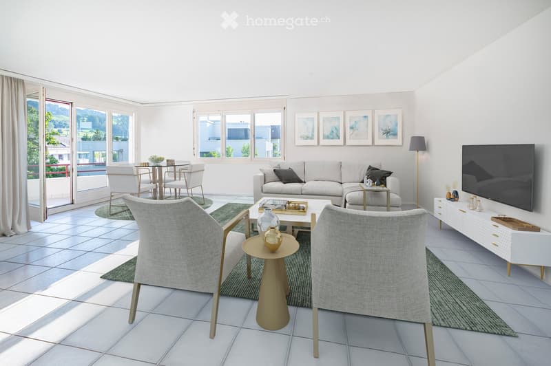 Bright living room with white walls, tiled floor, large windows, and a balcony. Features a grey sofa, coffee table, chairs, dining table, TV, and decorative items.