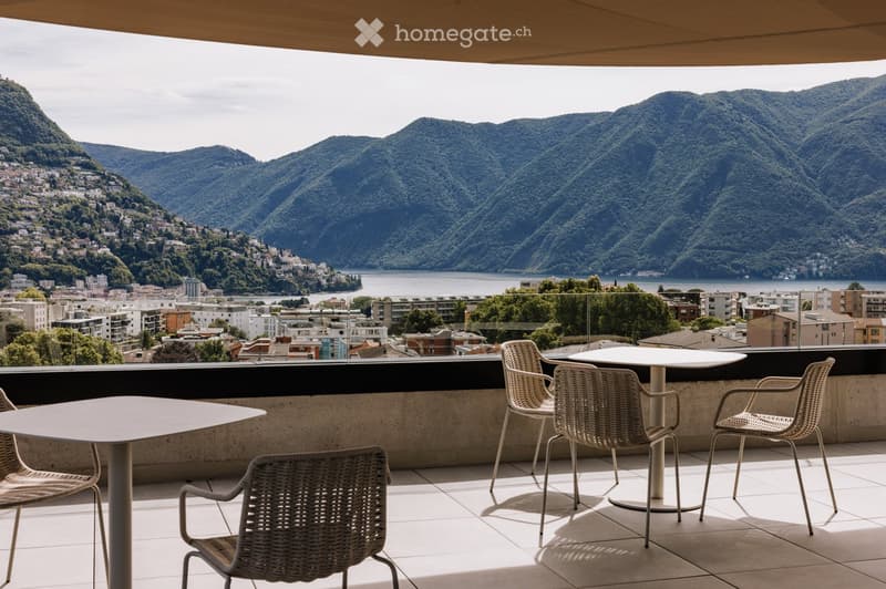 Balcony with a scenic mountain and lake view, featuring a white table and four wicker chairs.