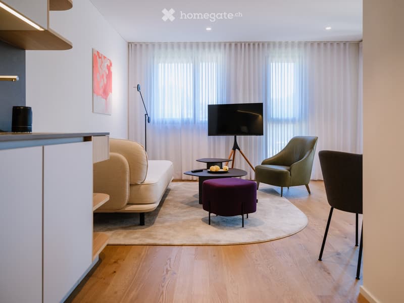 Modern living room with a beige sofa, green armchair, purple ottoman, coffee table, TV on a stand, floor lamp, and large windows with white curtains.