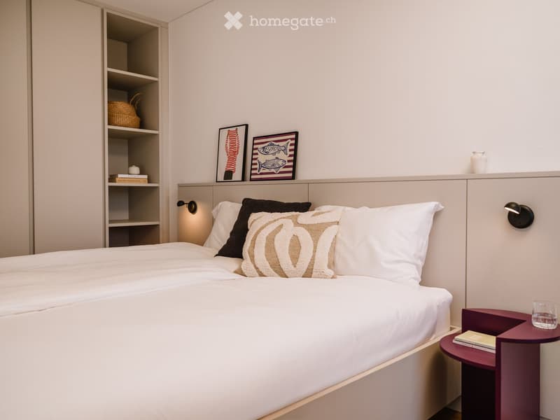 Modern bedroom with a neatly made bed, nightstand, and decorative items on shelves and walls.