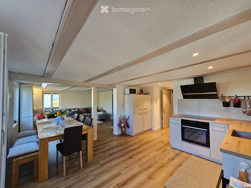 Open-plan living and dining area with wooden flooring, a dining table with chairs, a sofa, and a modern kitchen with white cabinets, an oven, and a microwave.