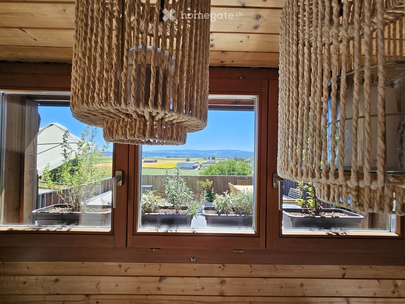 Wooden balcony with large windows, hanging rope light fixtures, and potted plants visible outside.