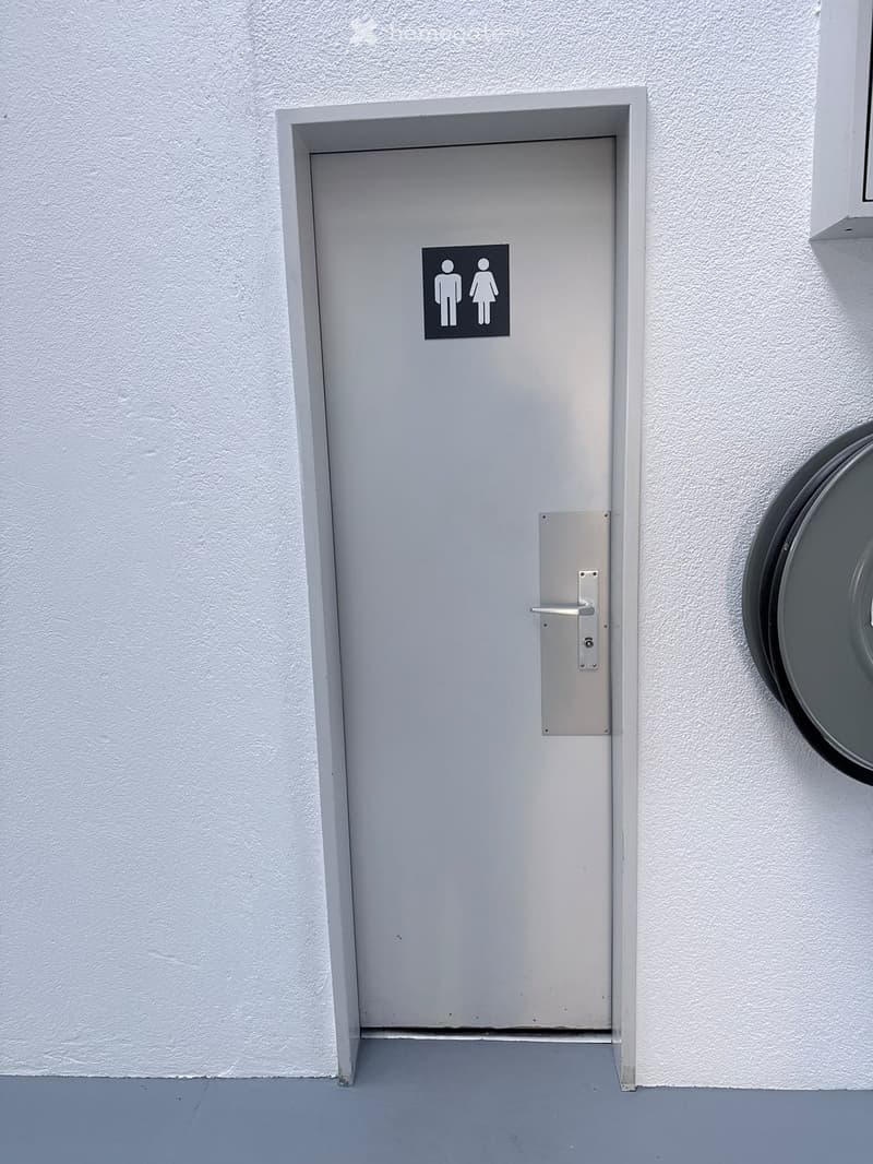 A closed grey restroom door with a male and female symbol sign, mounted on a white textured wall.