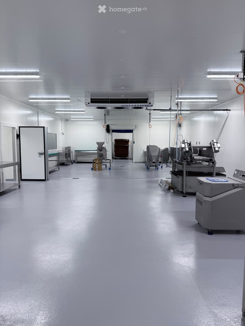 Clean, well-lit industrial room with stainless steel equipment, tables, and a large door leading to another area.