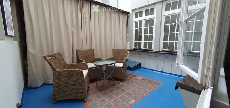 Balcony with blue painted floor, red and grey checkered tile area, wicker chairs, and a small round table.