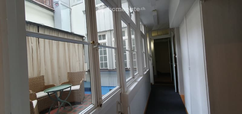 Balcony with wicker chairs and a small table, overlooking a pool area with blue tiles.