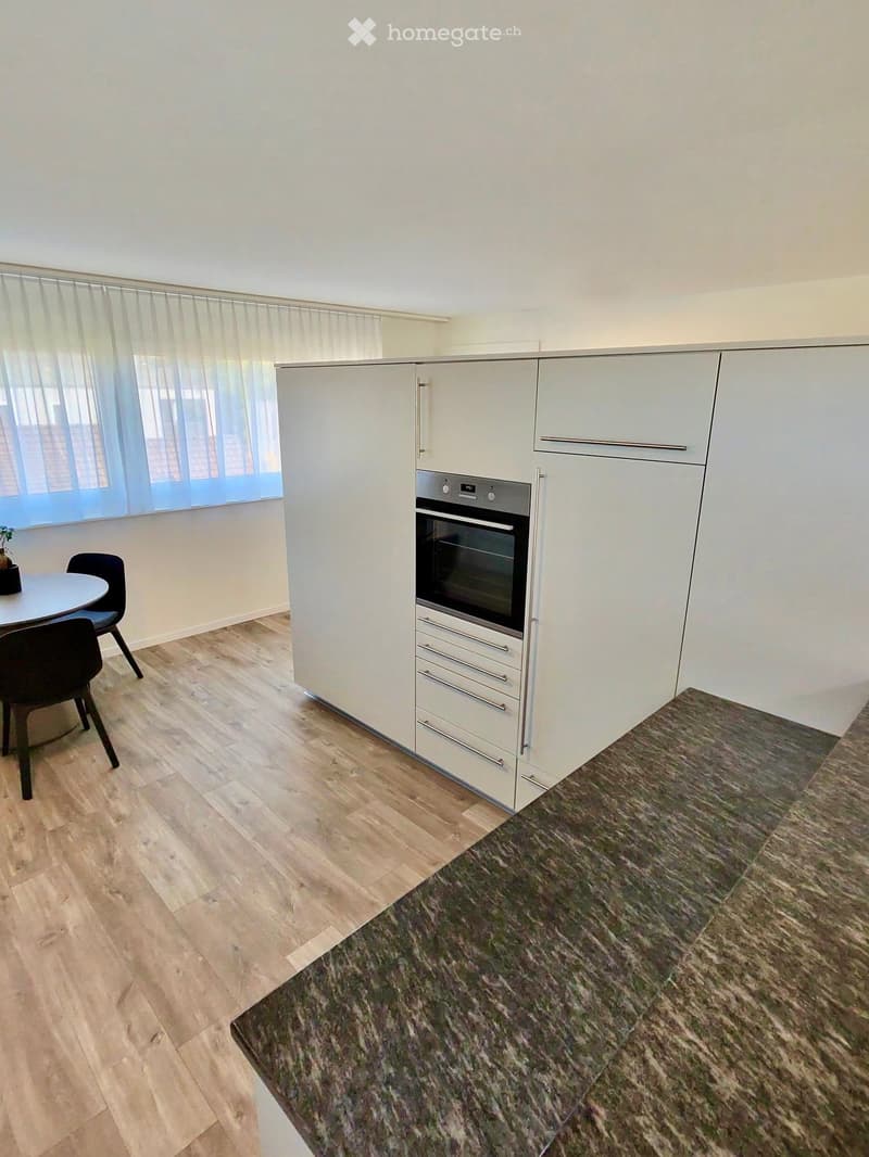 Modern kitchen with white cabinets, stainless steel oven, wooden flooring, and a small dining area with a round table and chairs.