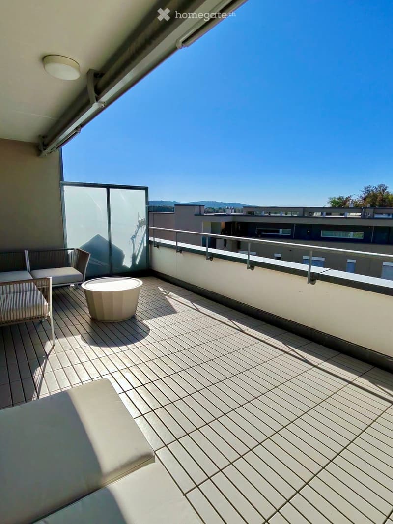 Balcony with wooden decking, white sofa, white chair, and a small round table.