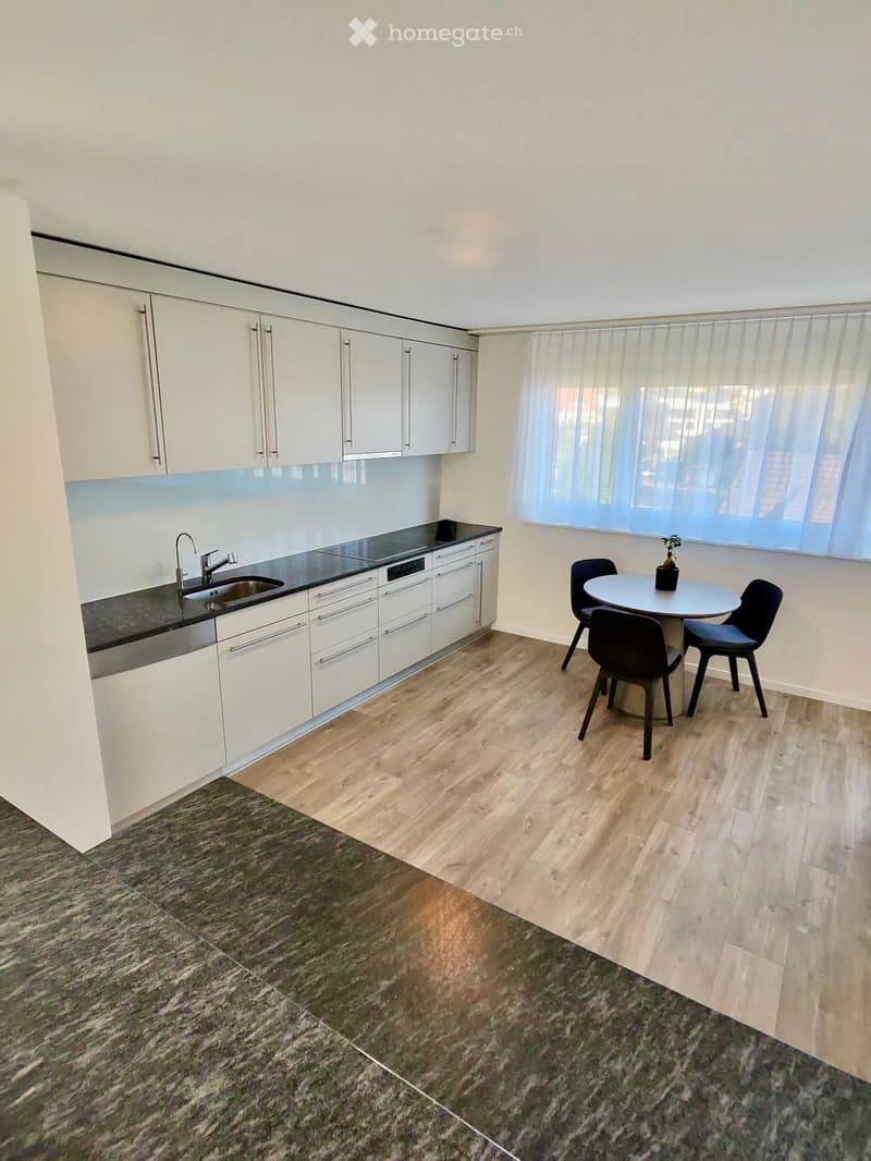 Modern kitchen with white cabinets, stainless steel sink, dishwasher, and a small dining area with a round table and chairs.