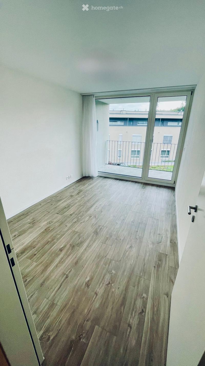 Empty room with light wooden flooring, white walls, and a large sliding glass door leading to a balcony area.