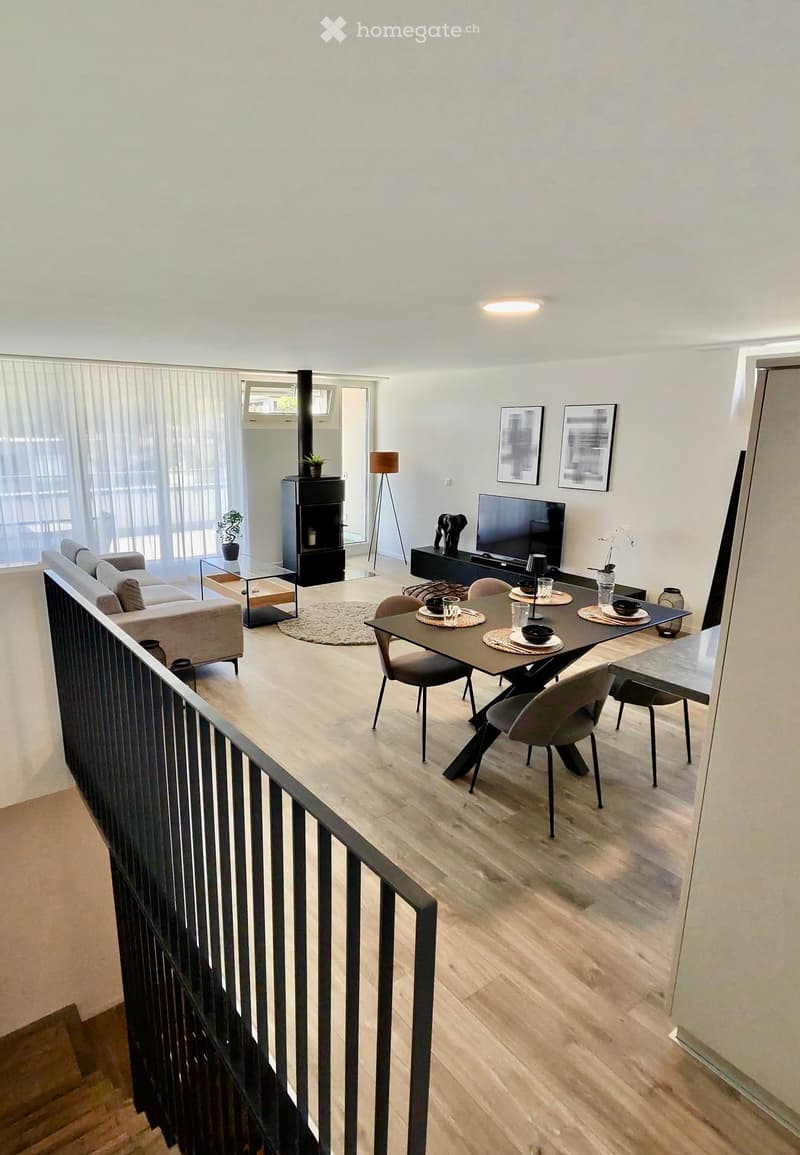 Modern living room with light wooden flooring, a grey sofa, a coffee table, a fireplace, a TV, a dining table with chairs, and a floor lamp.