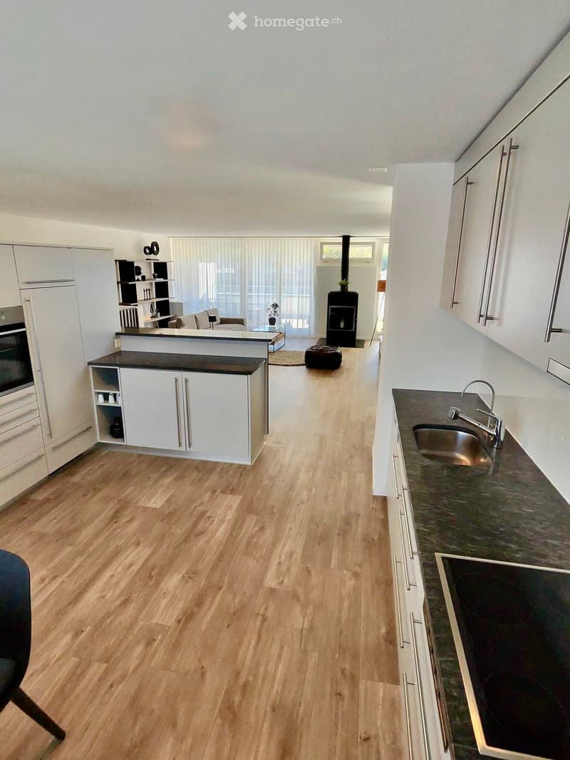 Open-plan kitchen and living area with light wooden flooring, white cabinets, a central island, a sink, and a fireplace.