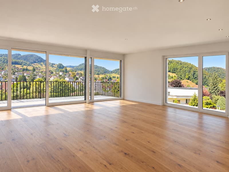 Bright, empty room with large sliding glass doors leading to a balcony, wooden floor, and scenic mountain view.