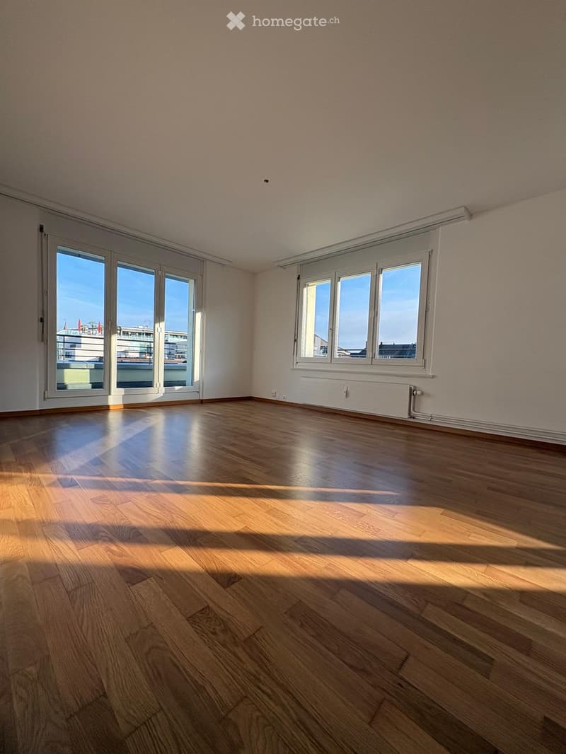 Empty room with wooden flooring, large windows, and sliding glass doors leading to a balcony.