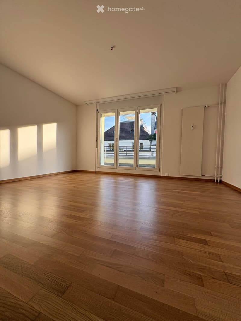 Empty room with wooden flooring, large sliding glass doors, and natural light from the left side.