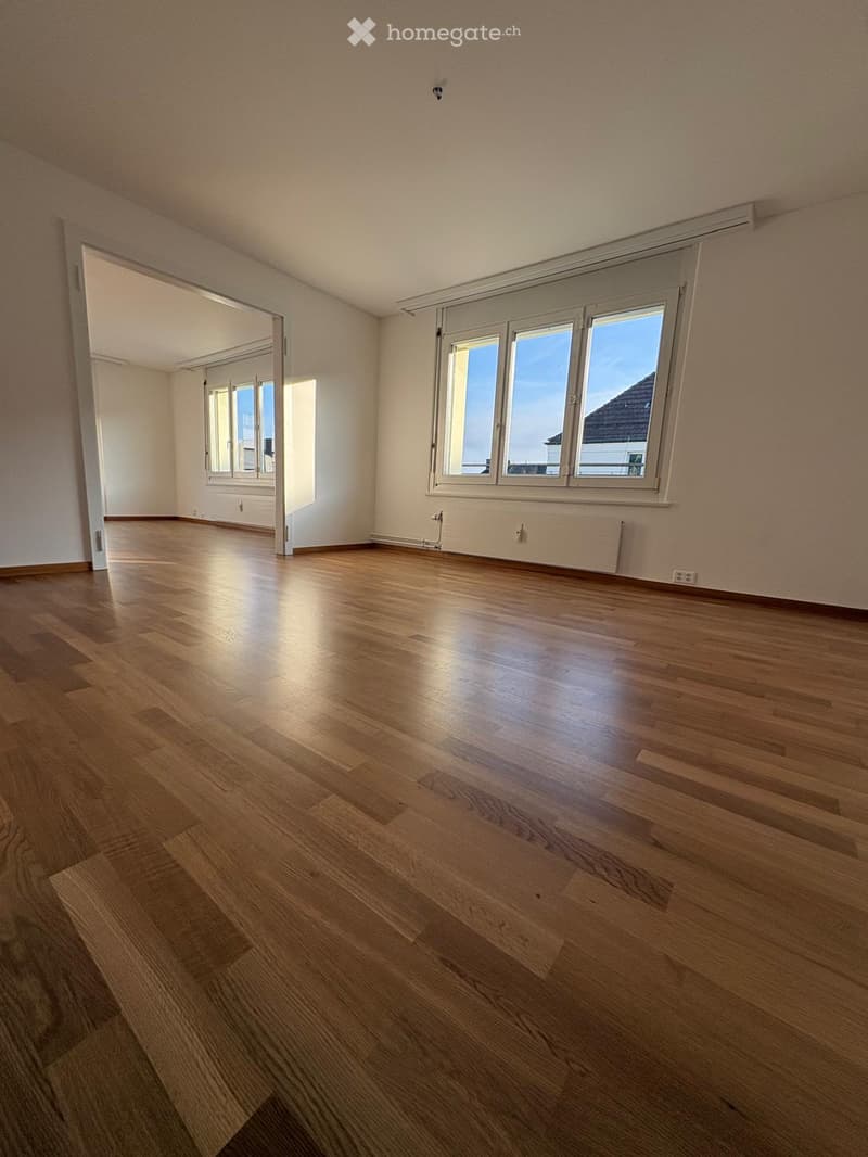 Empty room with wooden flooring, large windows, and white walls. No furniture or equipment present.