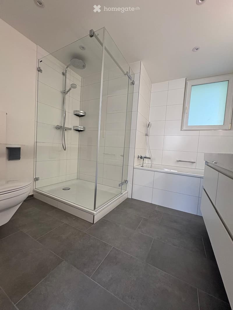Modern bathroom with a glass-enclosed shower, toilet, bathtub, and a window providing natural light.