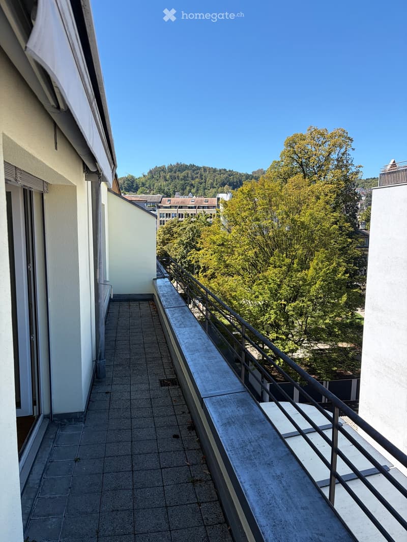 Balcony with tiled floor, metal railing, and scenic view of trees and buildings.