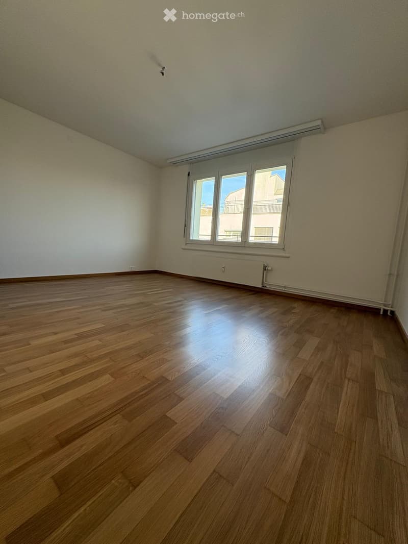 Empty room with wooden flooring, white walls, and a large window with white frame. No furniture or equipment present.